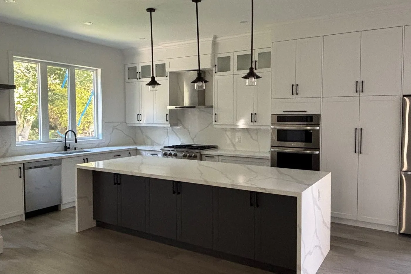 A finished kitchen with a marble waterfall island and pendant lights