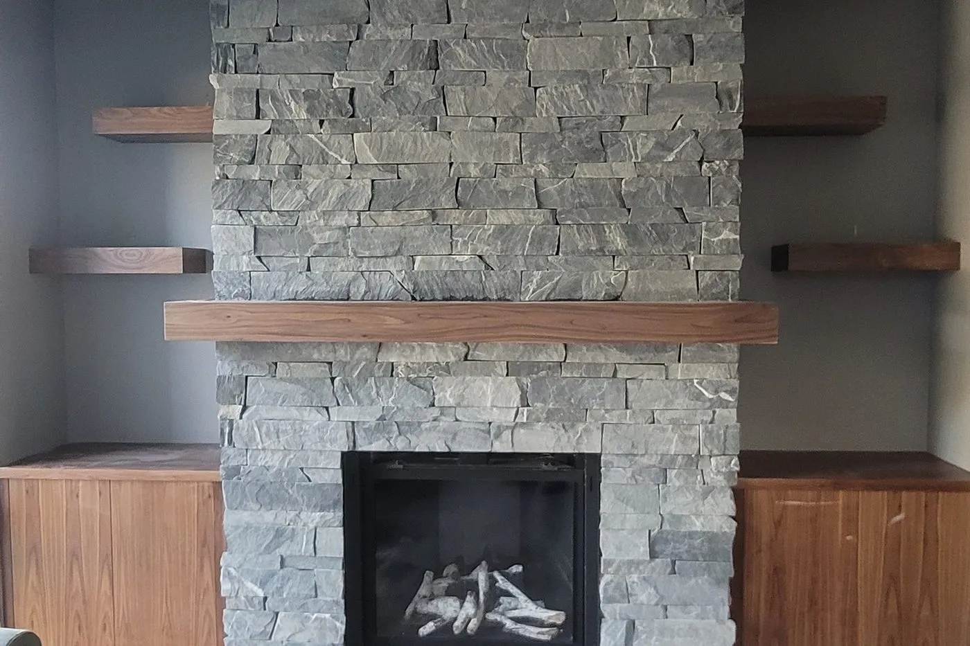 A stacked stone fireplace with a solid timber mantel and floating shelves