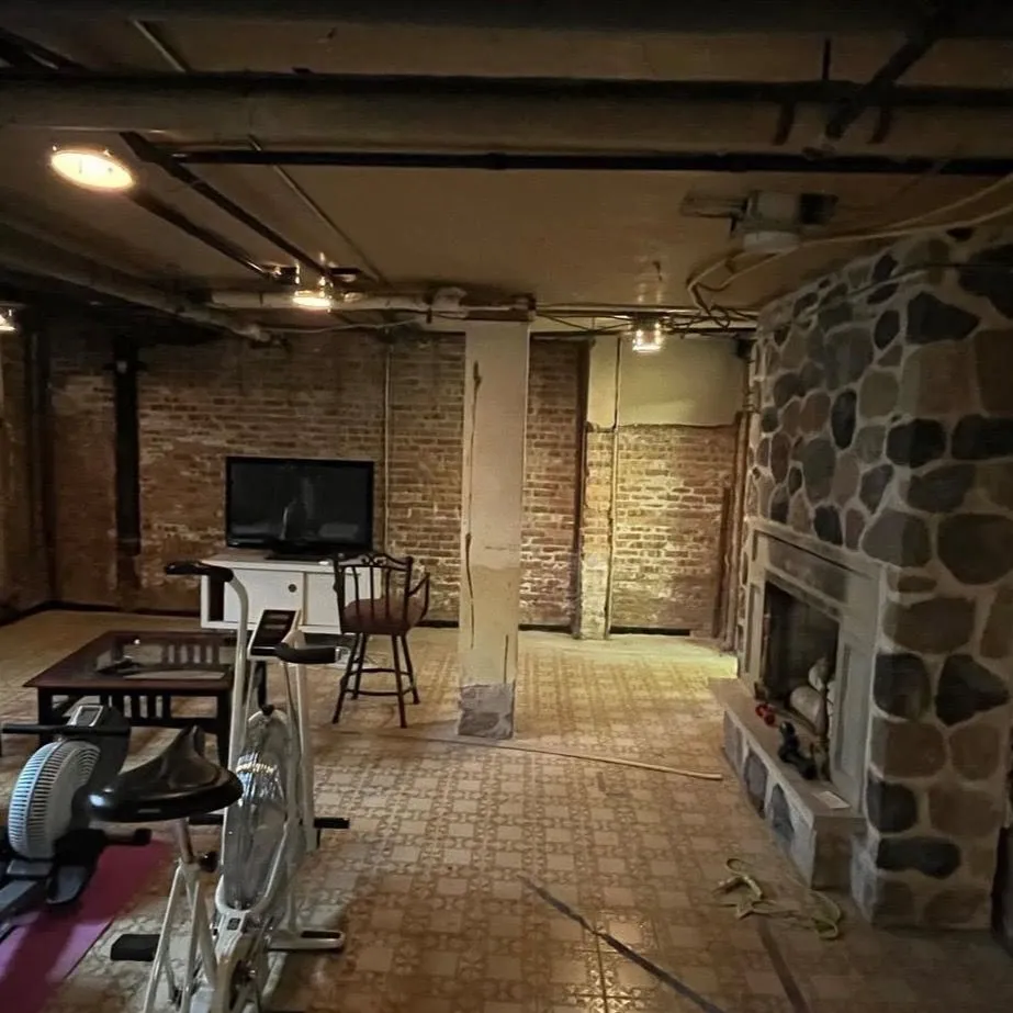 A basement in an Ontario century home with exposed brick and a fieldstone fireplace
